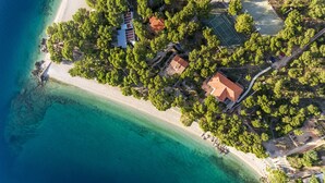 Luchtbeeld van een kustbezit met strand, bomen en gebouwen.