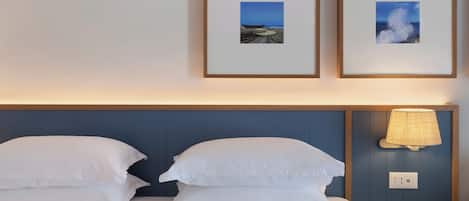 A hotel room with a bed, two pillows, a nightstand with a lamp, and two framed pictures on the wall.