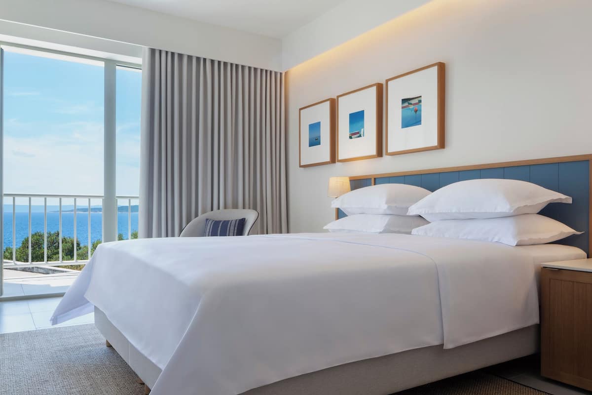 Habitación de hotel con una cama grande, una silla, un escritorio y vistas al mar.