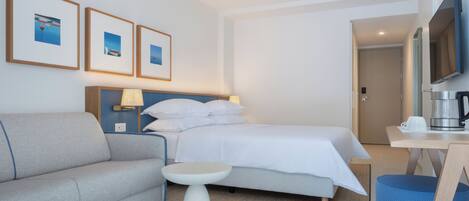 A hotel room with a bed, a sofa, a small table, a coffee maker, and framed pictures on the wall.