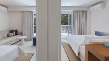 Habitación de hotel con cama, sofá, una mesita y balcón con vistas a árboles.