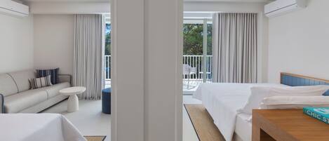 A hotel room with a bed, a sofa, a small table, and a balcony with a view of trees.