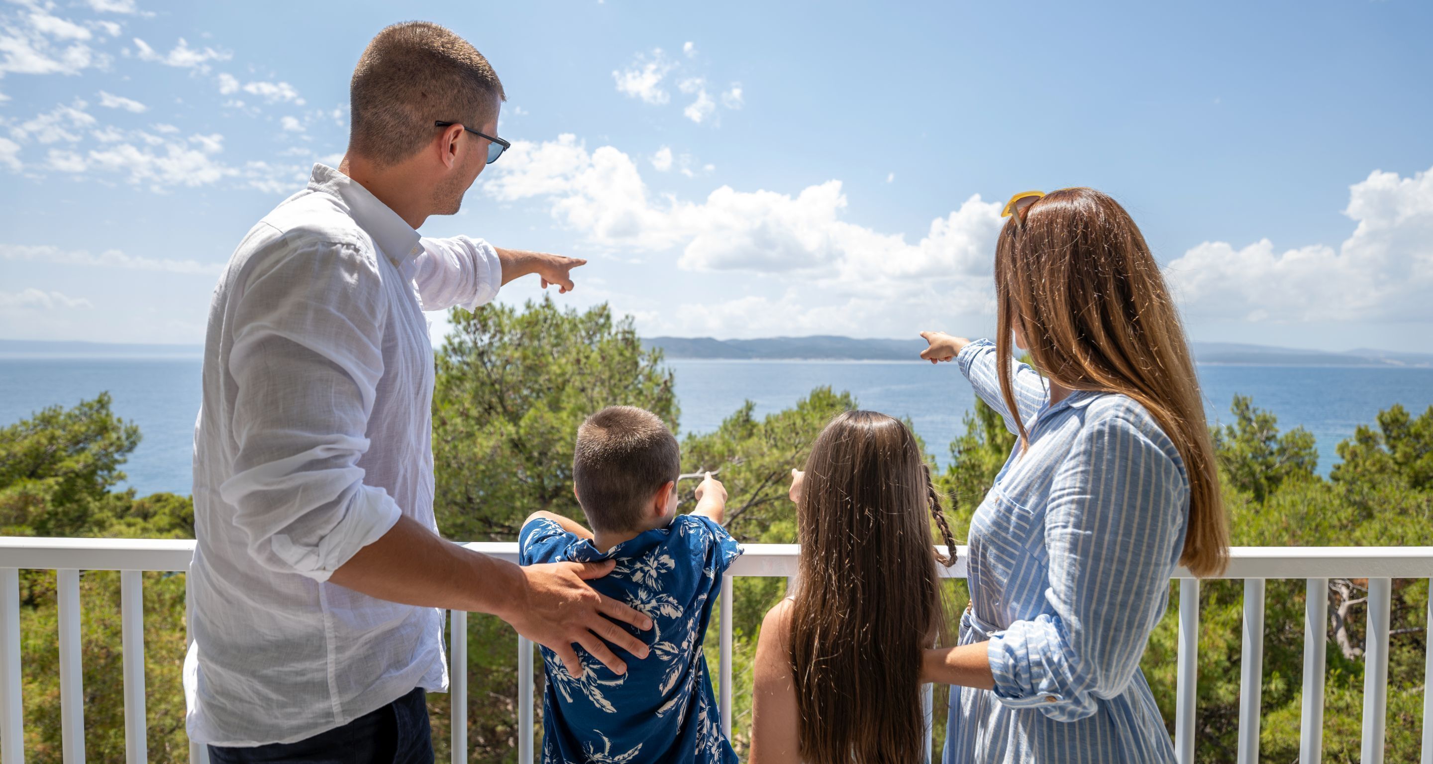 Una familia en un balcón que domina una vista panorámica de una masa de agua y tierra distante.