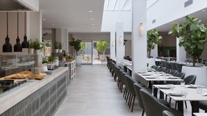 Een modern restaurant met een lange toonbank, meerdere tafels en potplanten.