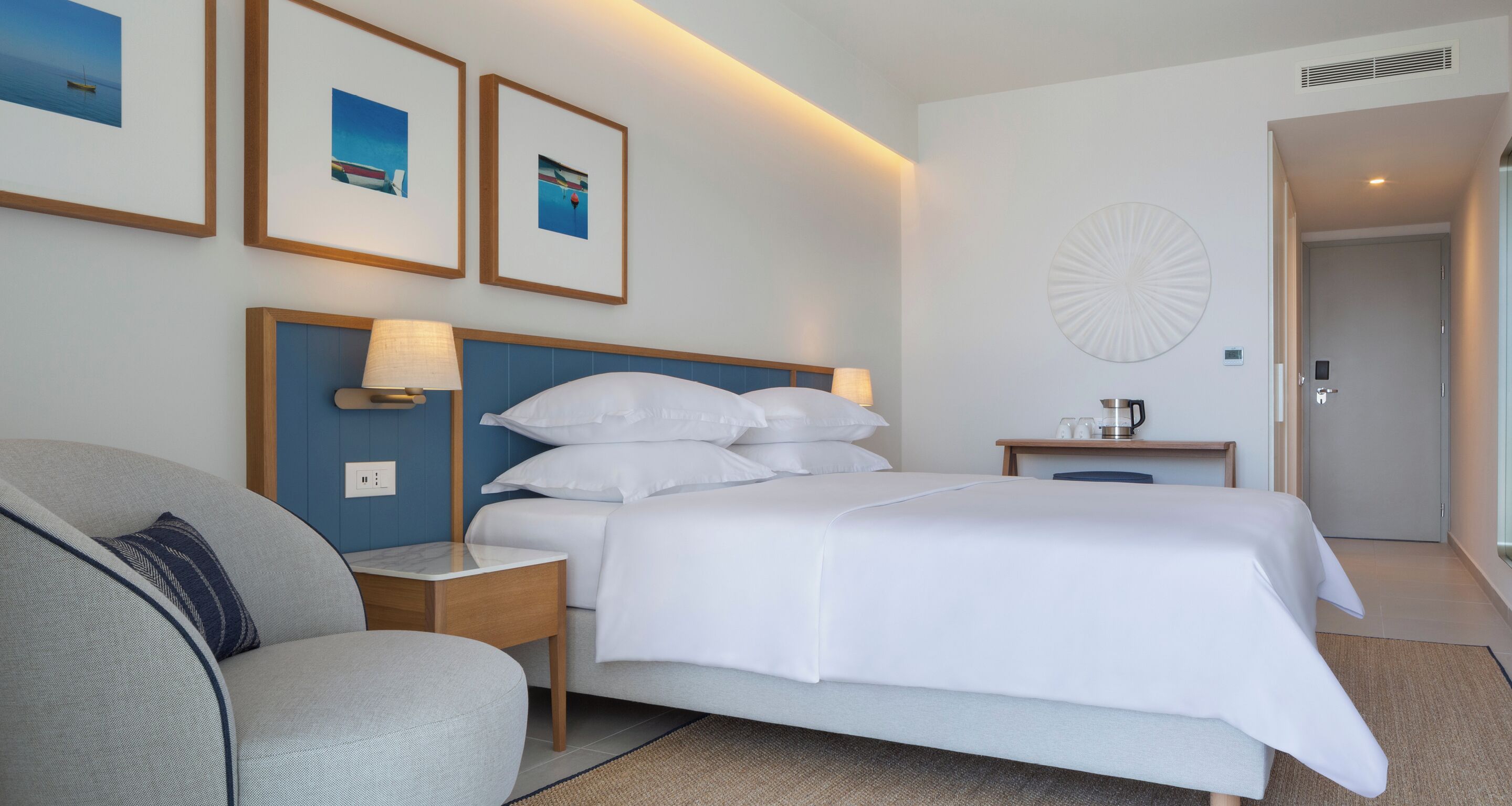 A hotel room with a bed, a nightstand, a lamp, a coffee maker, and framed pictures on the wall.