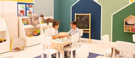 A children's playroom with white furniture, a chalkboard, and educational toys.