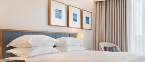 A hotel room with a bed, pillows, a chair, a nightstand, and framed pictures on the wall.