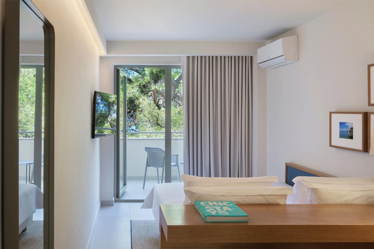 Habitación de hotel con cama, escritorio con lámpara, una silla y vistas al exterior a través de una puerta corredera.