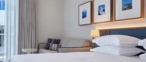 Una habitación de hotel con una cama, un sofá, una mesita y una lámpara. Hay tres cuadros enmarcados en la pared.