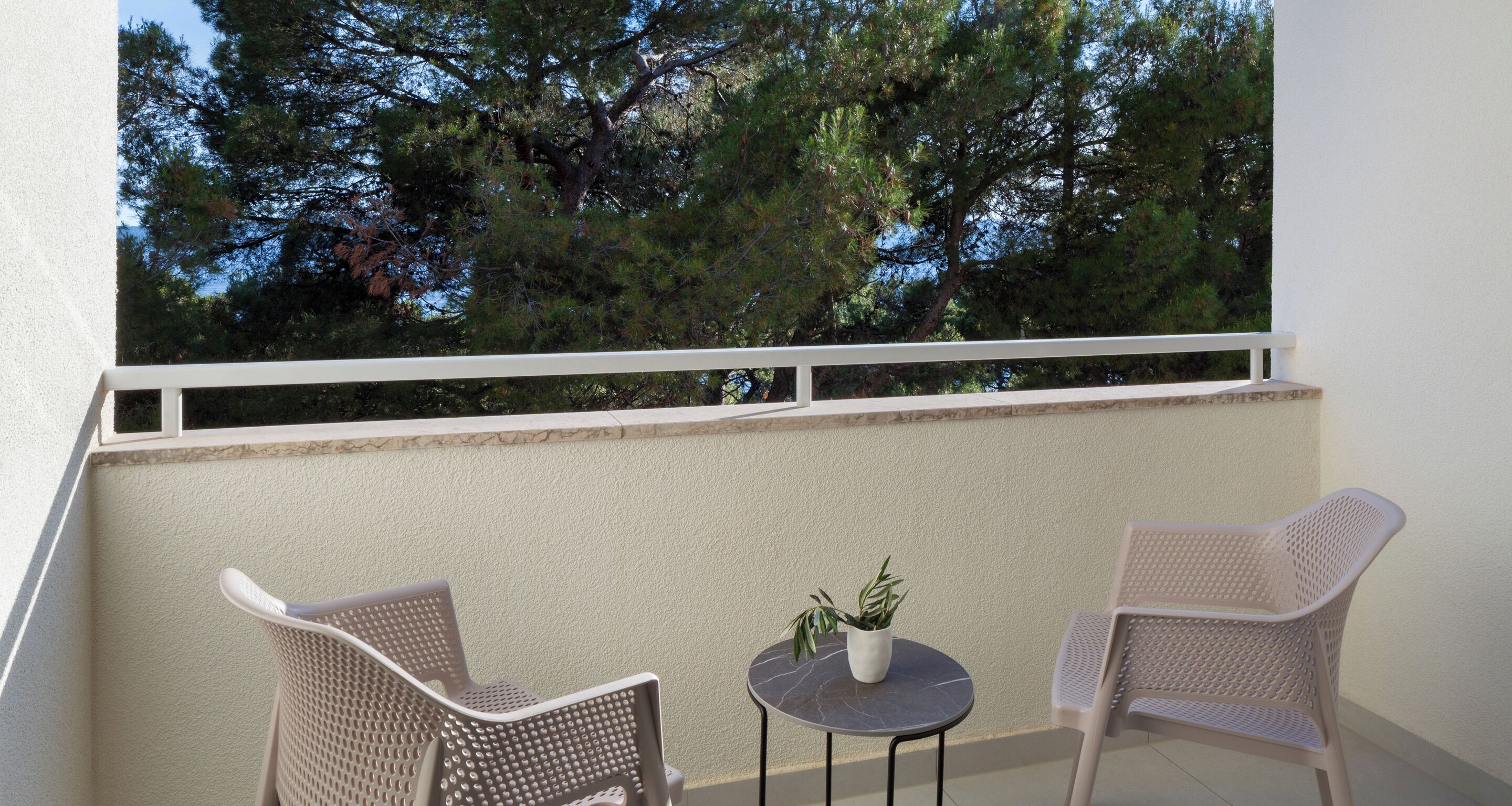 Un balcon avec deux fauteuils en osier et une petite table ronde sur laquelle est posée une plante en pot.