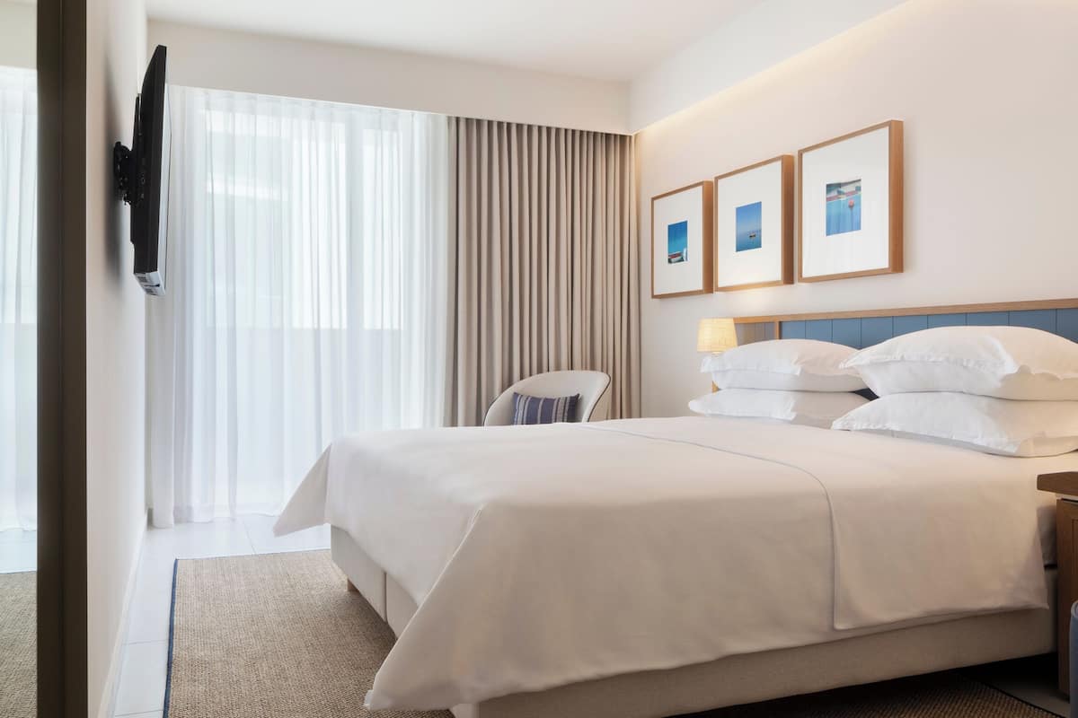 Habitación de hotel con cama, escritorio, silla, televisor montado en la pared y ventana con cortinas.