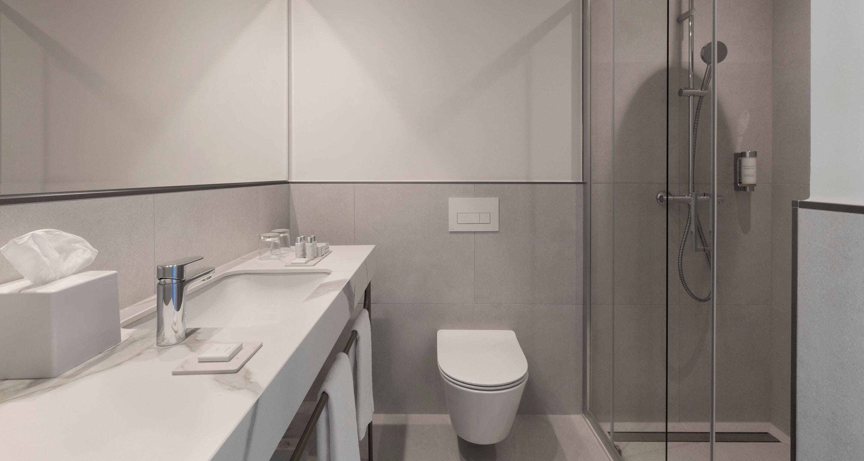 A modern bathroom with a glass-enclosed shower, a white sink with a marble countertop, and a toilet.