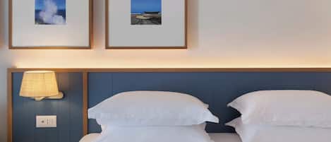 A hotel room with a bed, two pillows, a wall-mounted lamp, and two framed pictures of a beach scene.