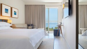Een hotelkamer met een groot bed, een bureau, een stoel en uitzicht op zee.