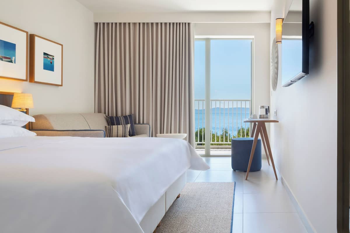 Habitación de hotel con una cama grande, un escritorio, una silla y vistas al mar.