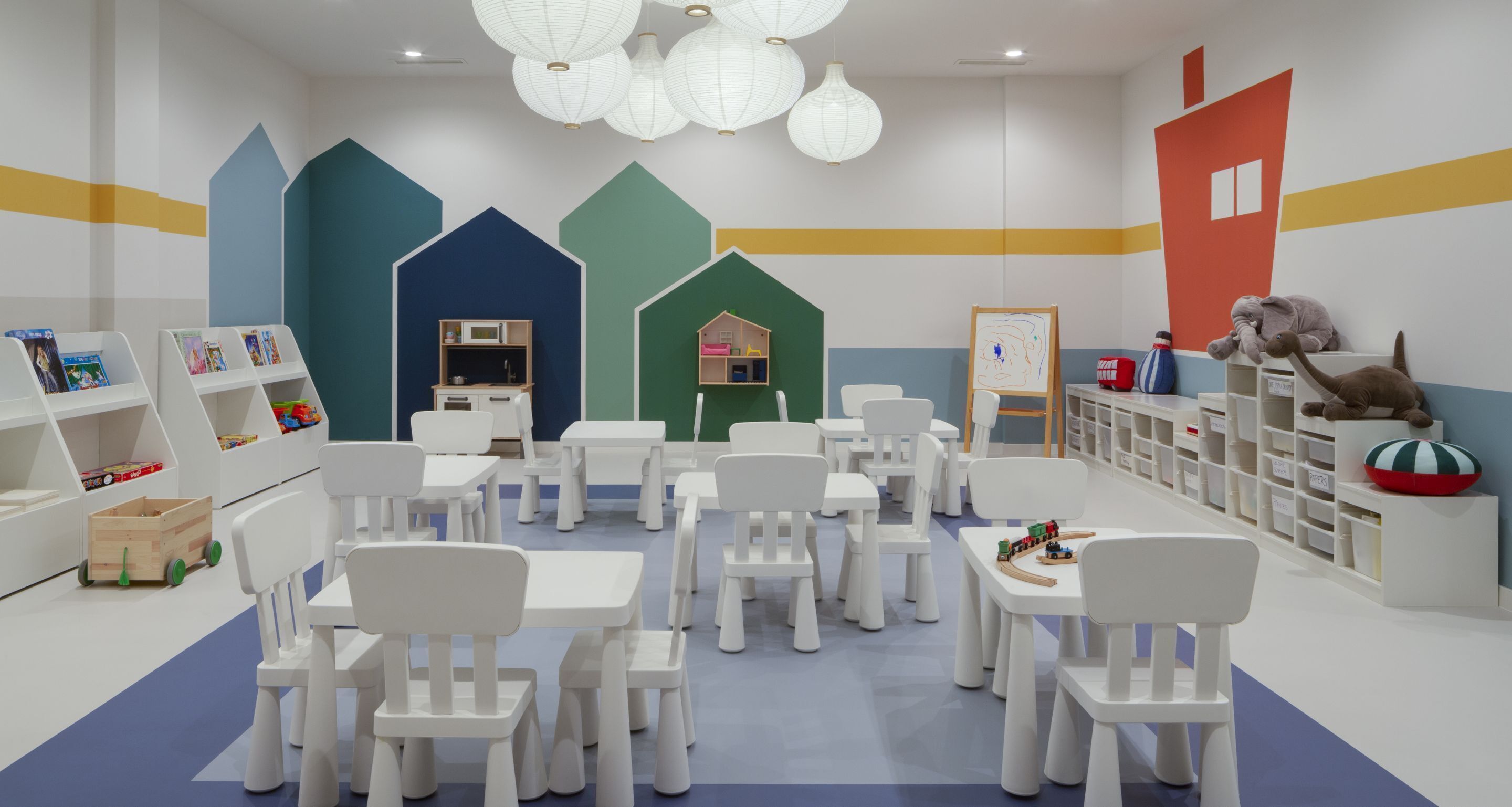 Une salle de jeux pour enfants avec des meubles blancs, des murs aux couleurs vives et divers jouets.