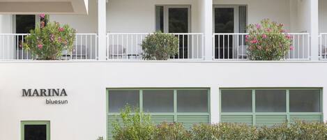 A two-story building named 'MARINA bluesun' with balconies, green shutters, and potted plants.