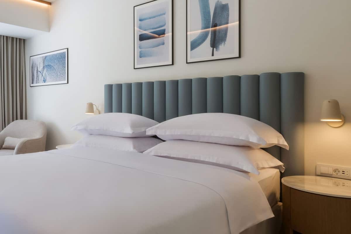 A modern hotel room with a large bed, a bedside table, a chair, and artwork on the walls.