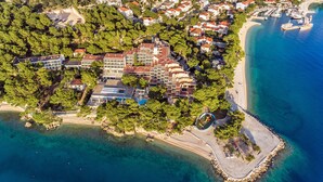 An aerial view of a coastal residential area with multiple buildings, a beach, and clear blue waters. - Bluesun Hotel Soline (Brela)