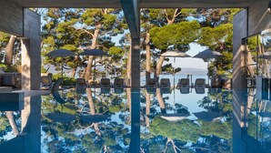A pool area with lounge chairs and umbrellas, surrounded by trees and a view of the sea. - Bluesun Hotel Soline (Brela)