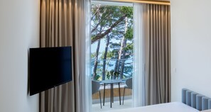 Habitación de hotel con una televisión montada en la pared, un balcón con mesa y sillas, y cortinas en las ventanas.