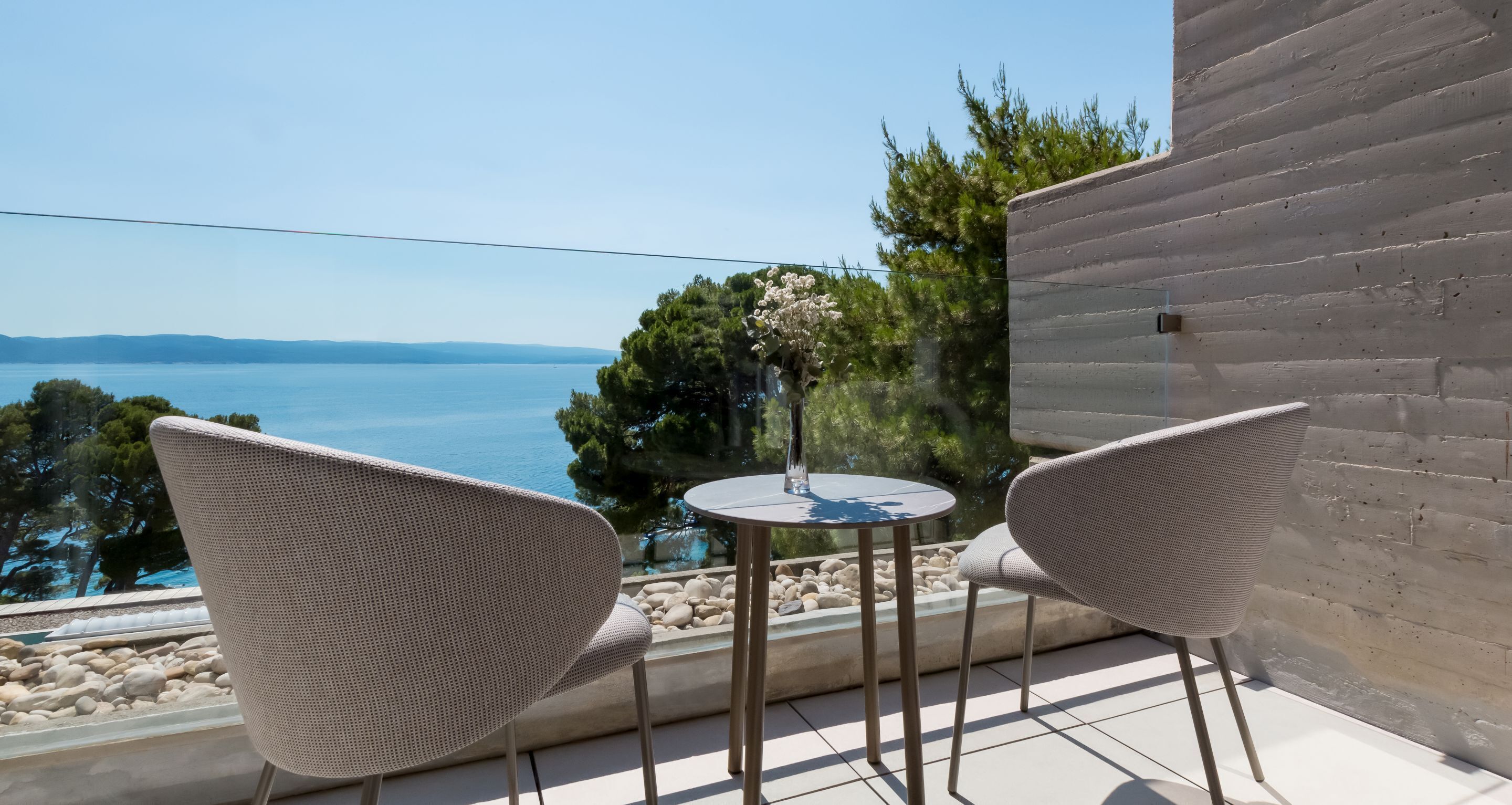 A balcony with two wicker chairs, a small round table, and a view of the sea.