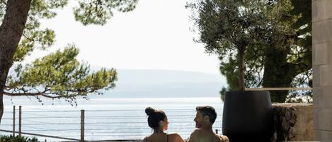 Una parella en una piscina nítida amb vistes al mar i a les muntanyes llunyanes.