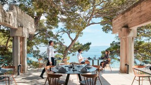 An outdoor dining area with round tables and chairs, overlooking a body of water. - Bluesun Hotel Soline (Brela)