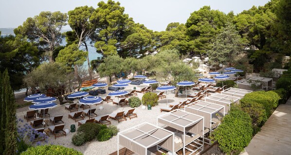 A beachside resort with rows of sun loungers and umbrellas, surrounded by dense trees and a view of the sea. - Bluesun Hotel Soline (Brela)