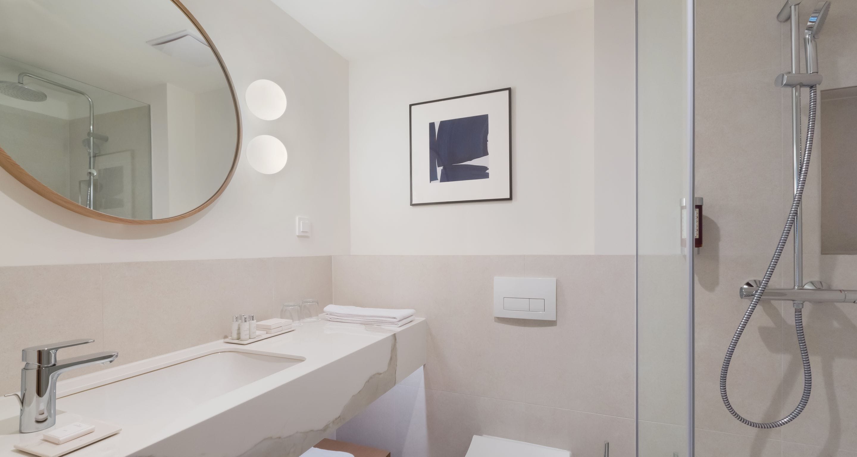 Une salle de bain moderne avec un grand miroir, deux lavabos, une douche et une œuvre d’art encadrée accrochée au mur.