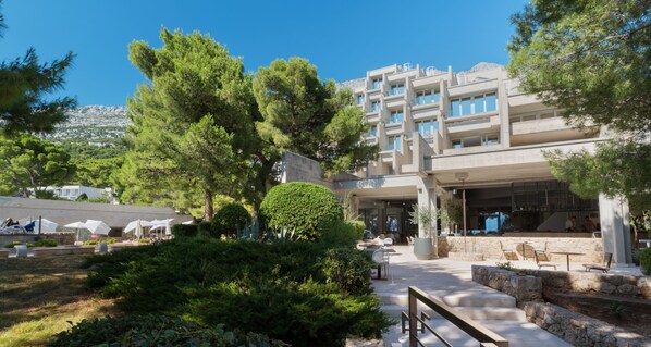 Un hotel moderno con asientos exteriores, piscina y montañas al fondo.