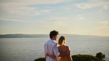 A couple standing by a body of water with a view of distant hills.