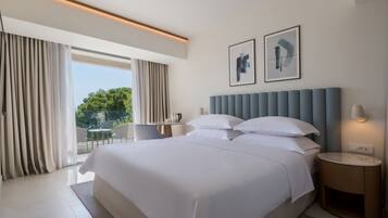 Habitación de hotel moderna con una cama grande, vistas a zonas verdes y un balcón.