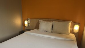 A neatly made bed with white linens, two pillows, and two wall-mounted bedside lamps.