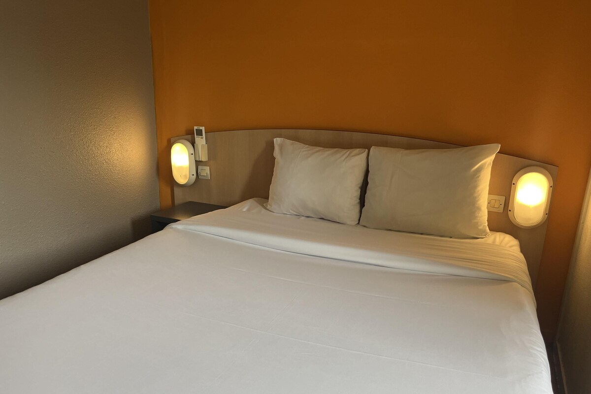 A neatly made bed with white linens, two pillows, and two wall-mounted bedside lamps.
