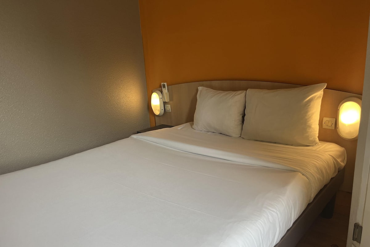 A single bed with white bedding, a headboard with a light switch, and two wall-mounted light fixtures.