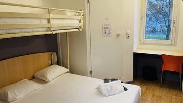 Een hotelkamer met een stapelbed, een bureau met een stoel en een raam met uitzicht op bomen.