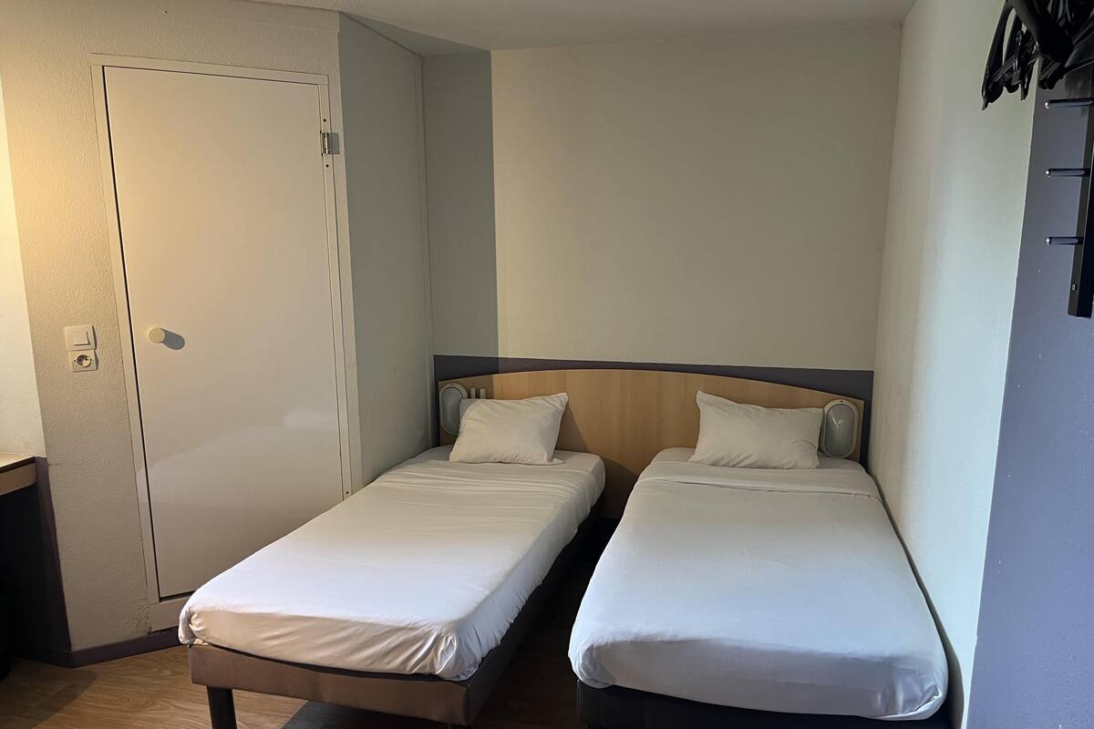 A small room with two single beds, a door, and a wall-mounted shelf.