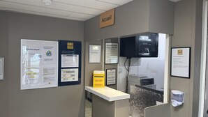 A hotel reception area with a counter, informational posters, a television, and a sign indicating the location.