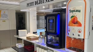 A self-service beverage station with a Tropicana dispenser, a coffee machine, and a sign reading 'PETIT DEJEUNER'.