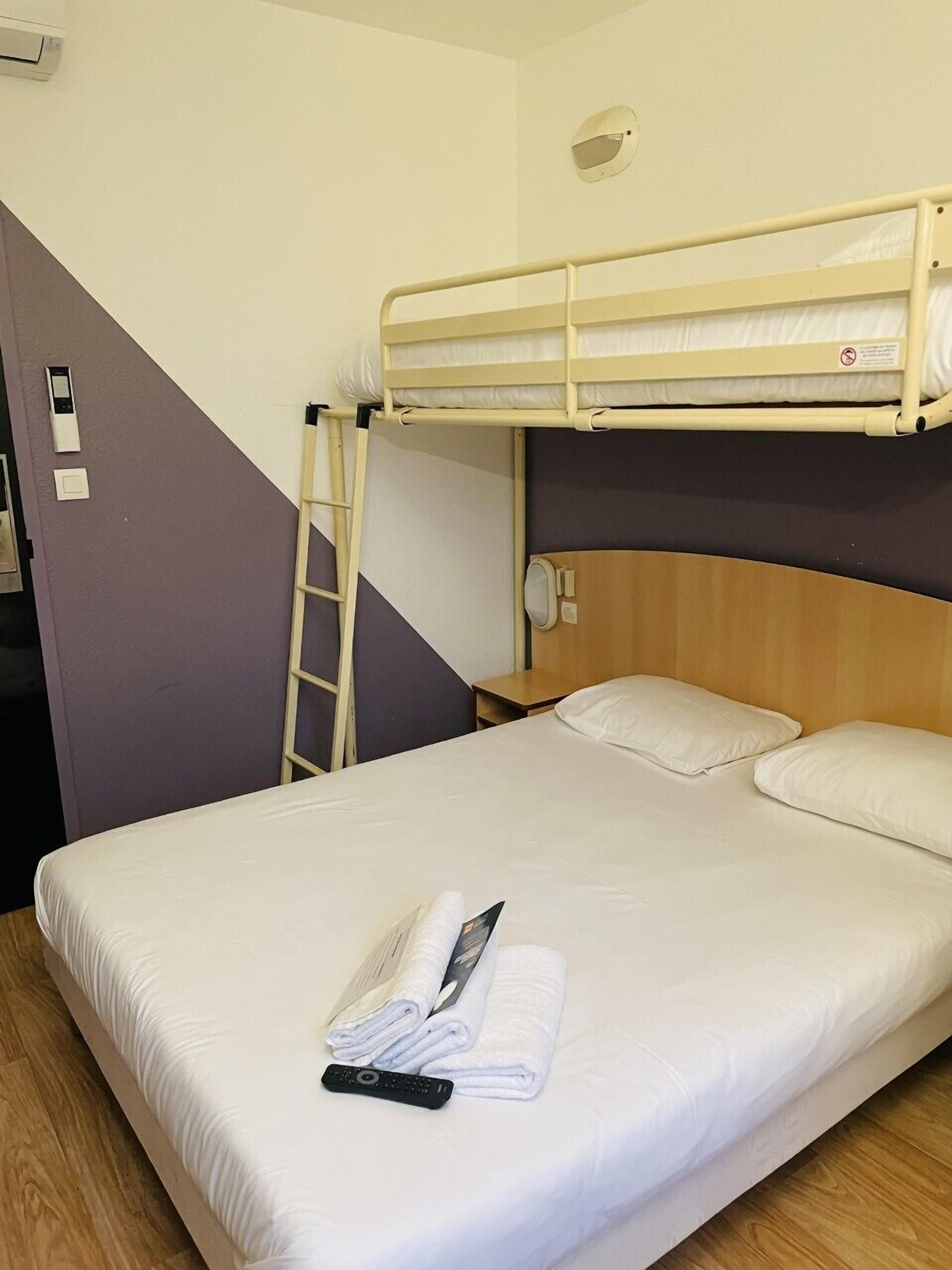 Een eenpersoonskamer met een bed boven elkaar, een houten hoofdbord, een nachtkastje, een afstandsbediening en een opgevouwen handdoek op het bed.