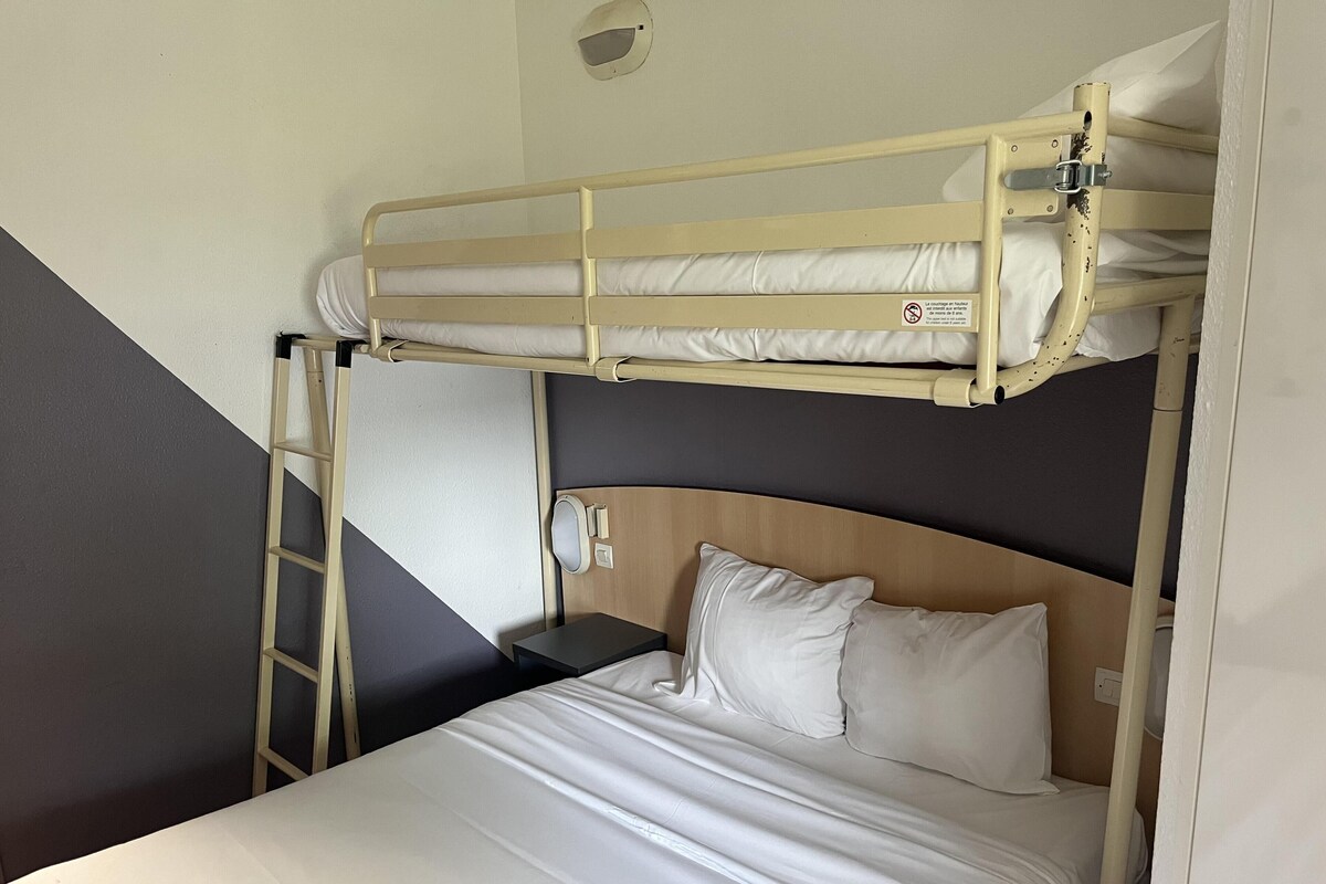 A bunk bed with a ladder, a bedside table, and a wall-mounted light fixture.