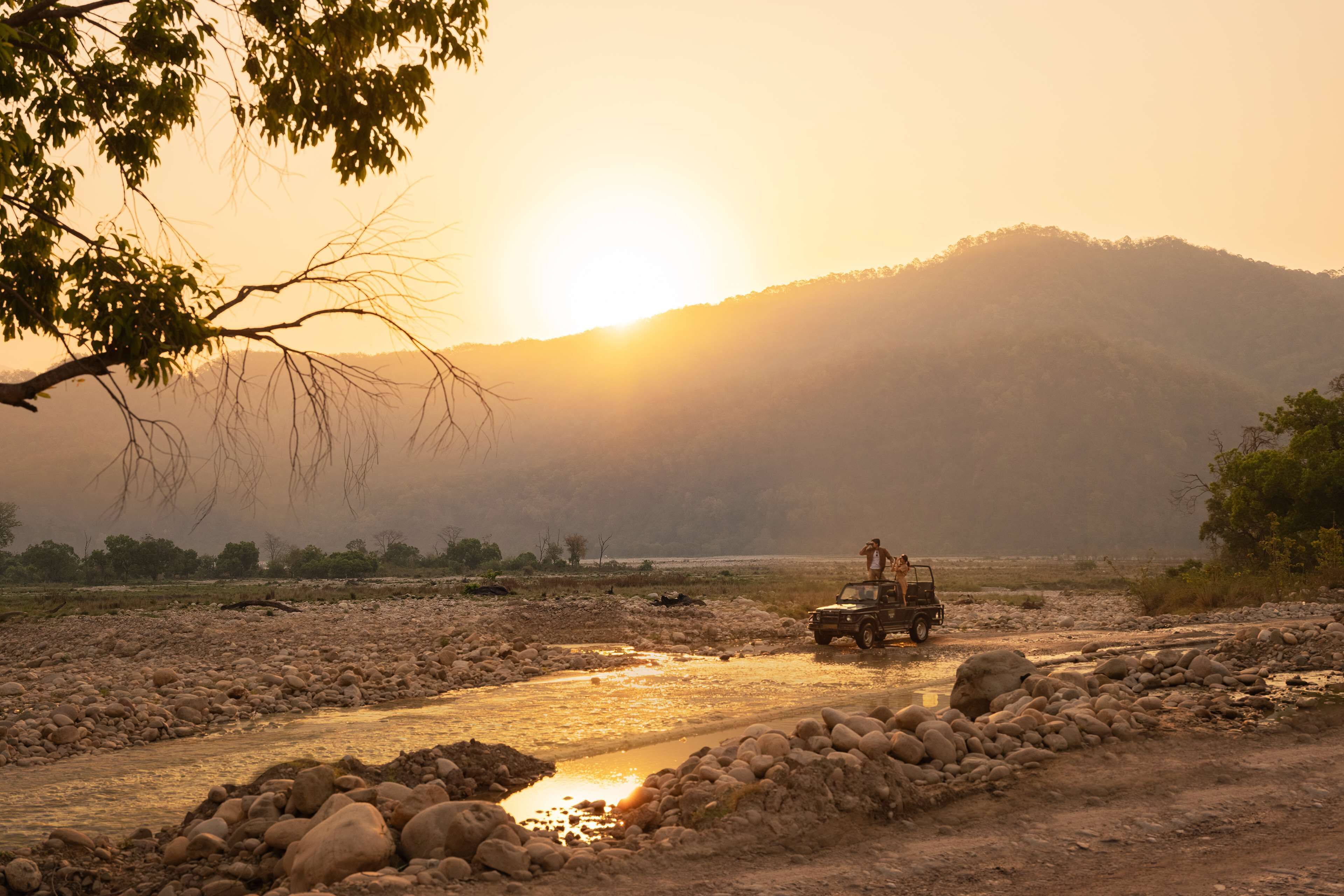 A jeep on a rocky path with a river and hills in the background.