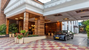 Entrada de hotel con piso a cuadros, un coche negro estacionado adelante y un área cubierta con columnas y plantas.
