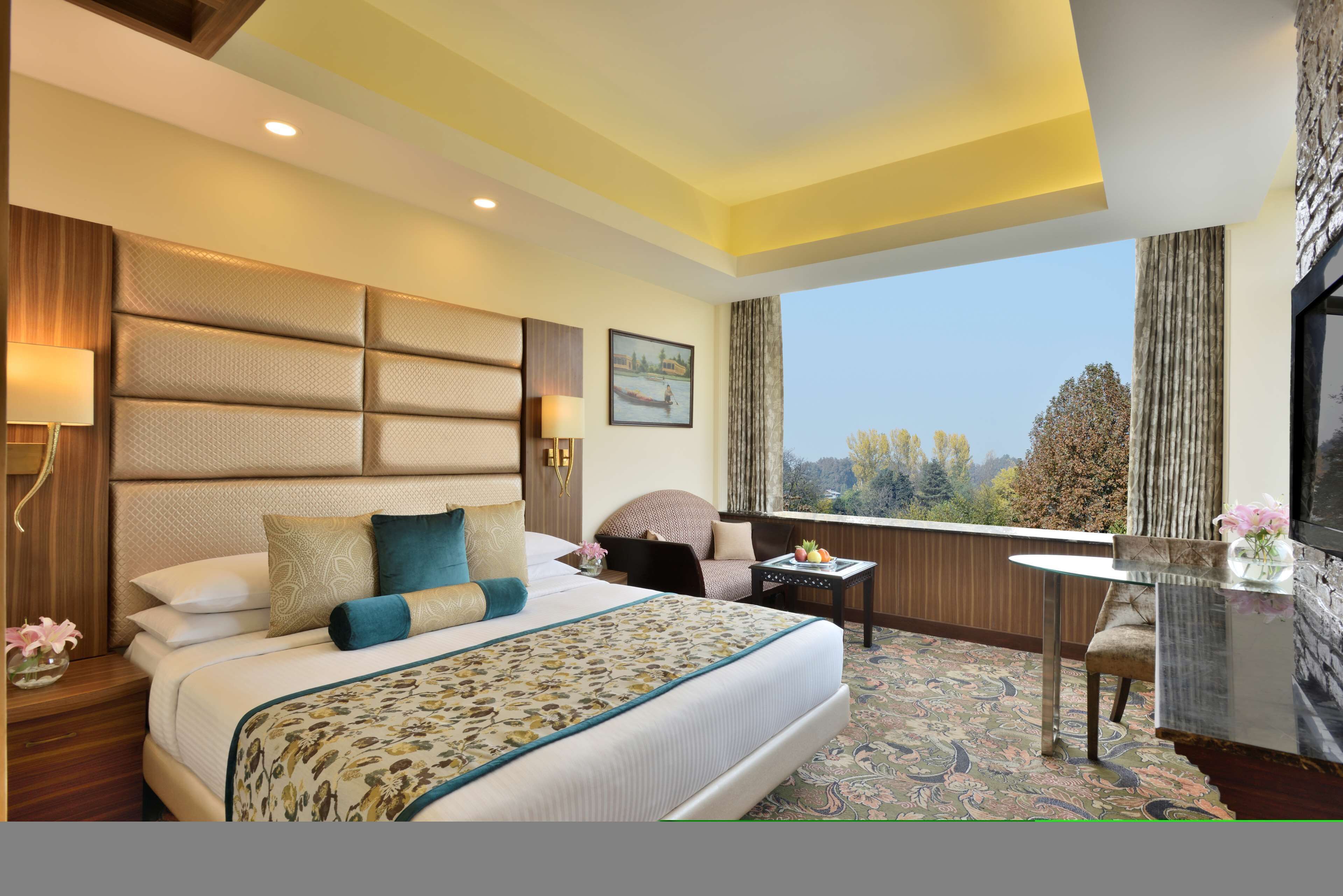 A hotel room with a large bed, a desk, a chair, and a view of the outdoors.
