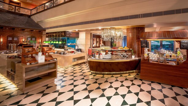 Un vestíbulo de hotel con piso a cuadros, un área de bar central y un bufé con diferentes opciones de comida.