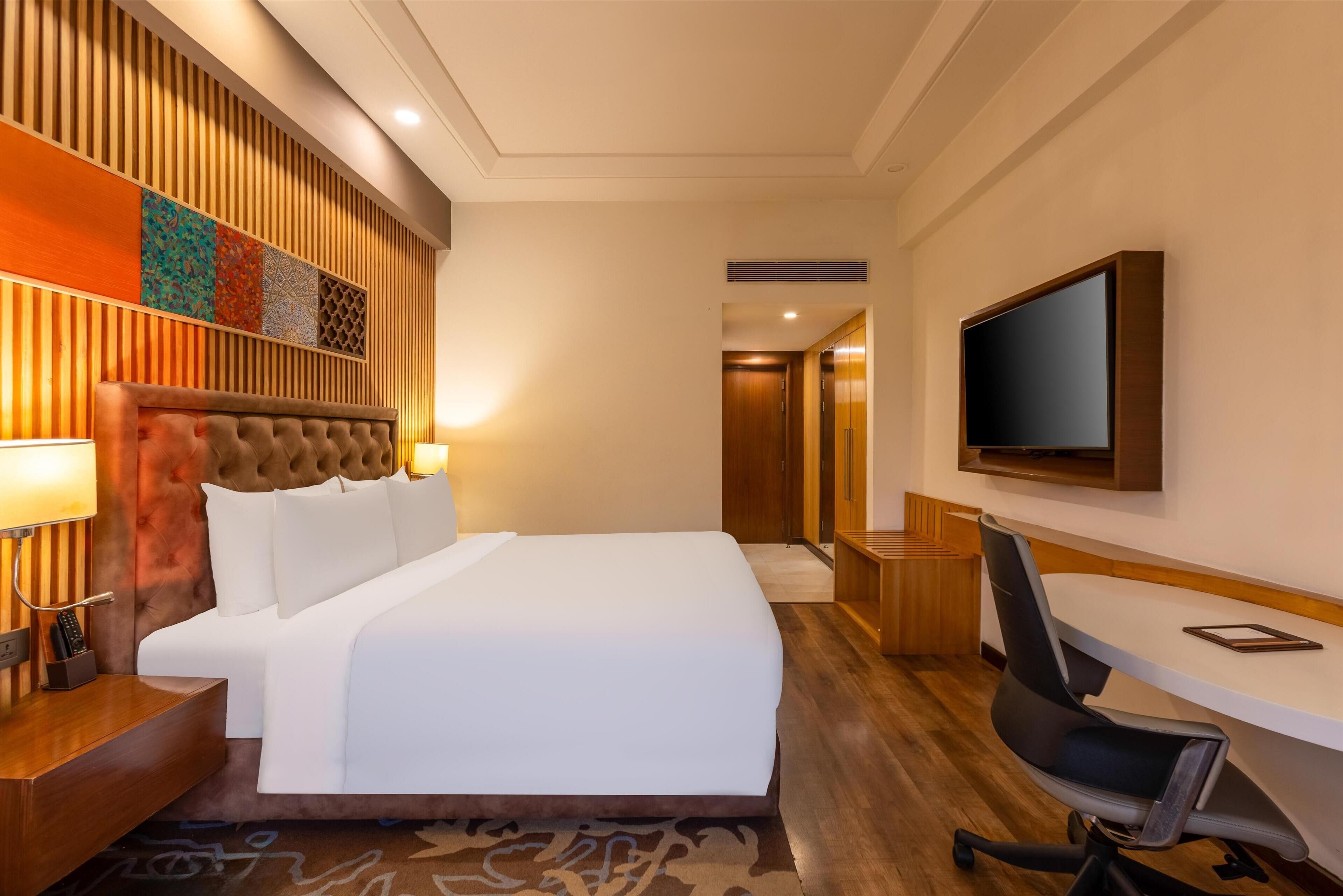 Habitación de hotel con una cama grande, un escritorio con silla, televisión y pared de paneles de madera.