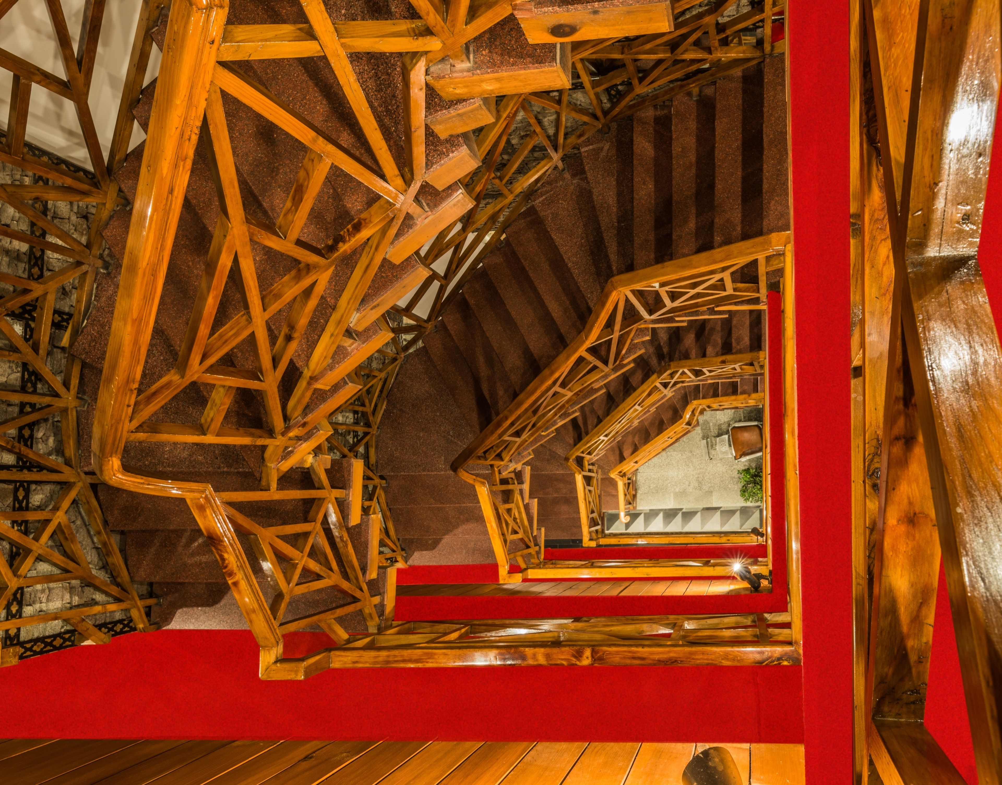 Una escalera de madera con alfombra roja, que conduce a una habitación con pared de piedra y una ventana.