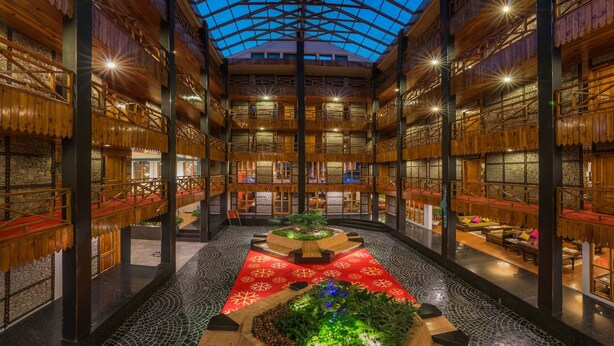 A spacious atrium with a high ceiling, wooden beams, and a central garden area. - Honeymoon Inn (Manali)