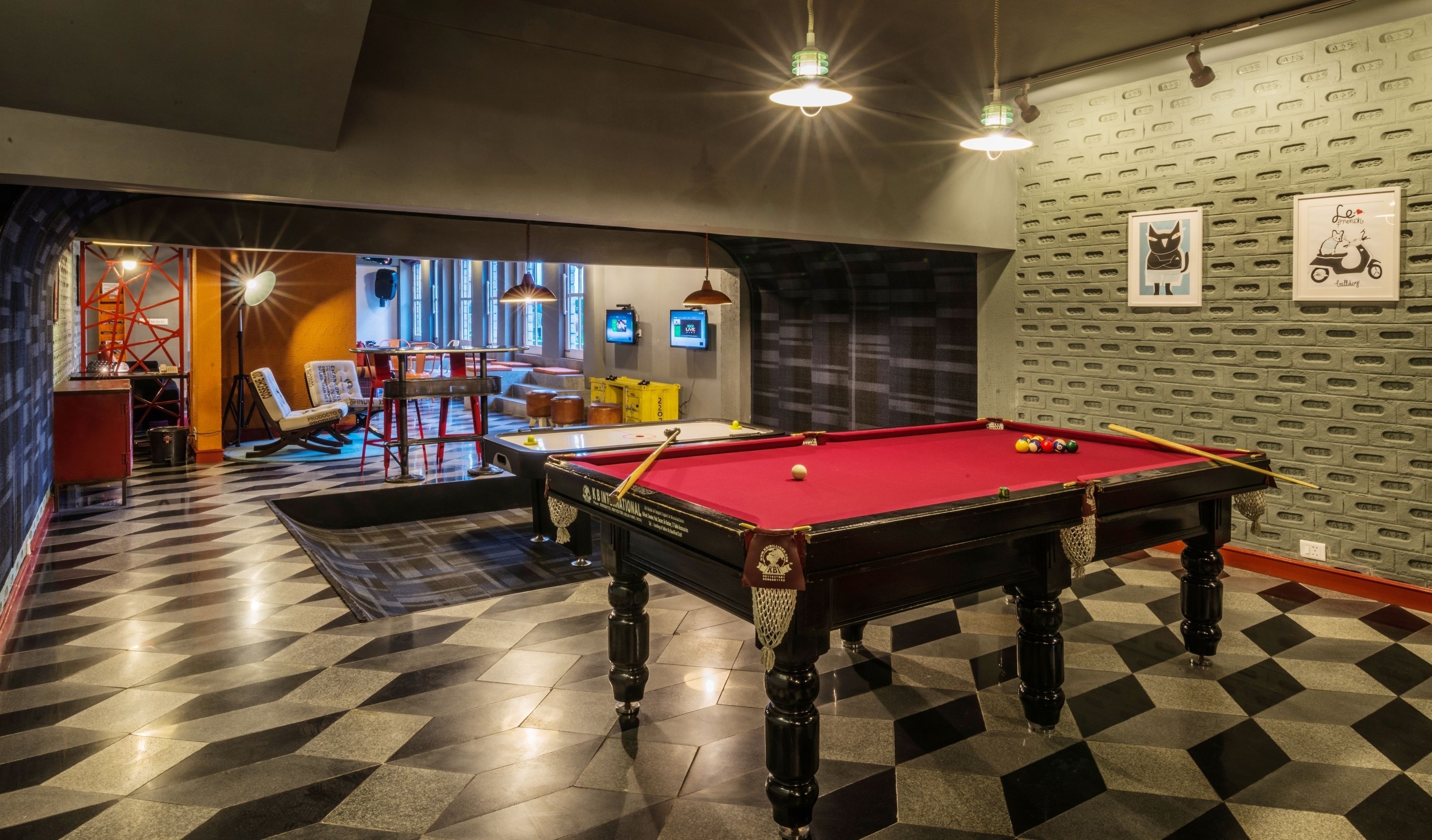 Una mesa de billar en una sala con piso a cuadros, una mesa de pool y una pared con cuadros enmarcados.
